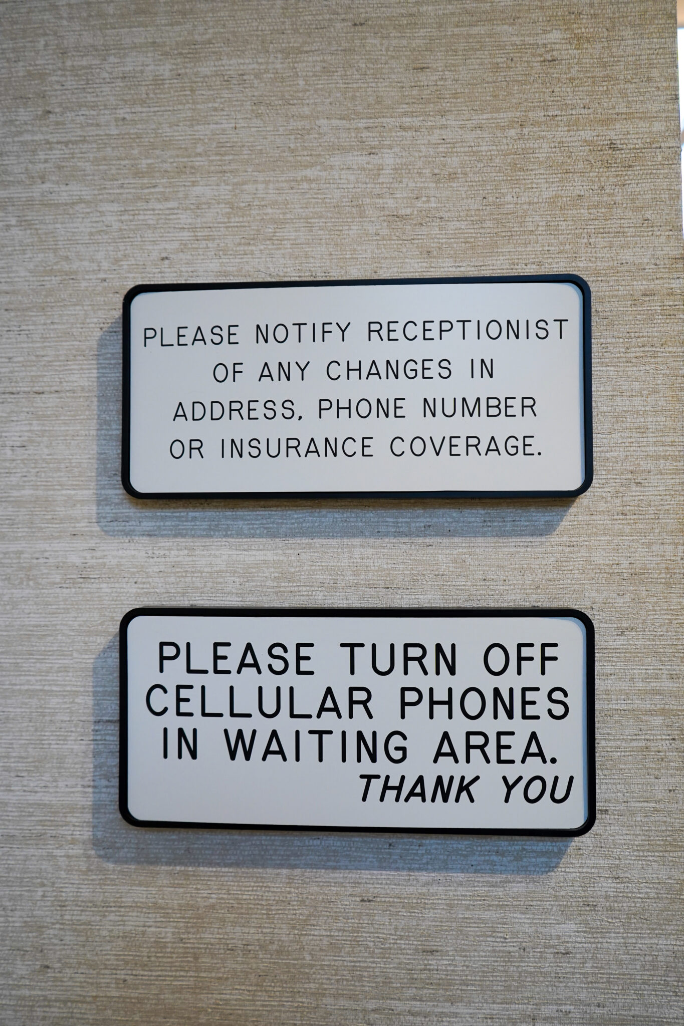 Two rectangular white signs with black borders mounted on a textured wall inside a dental office waiting area with patient policy instructions.