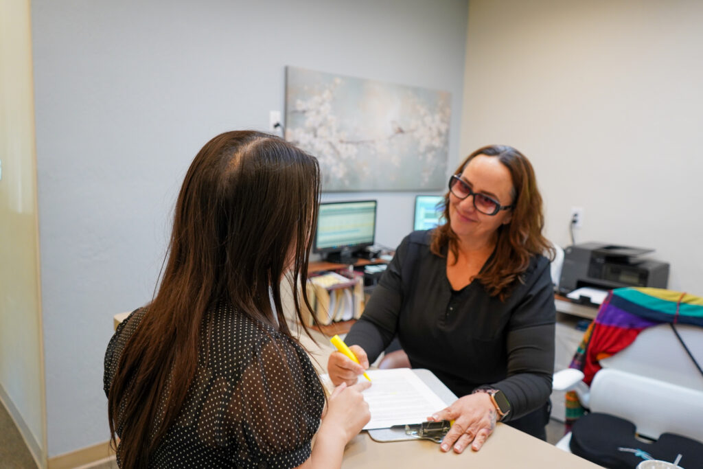 A friendly receptionist in black scrubs guides a female patient through paperwork at the front desk of Zhao Dental of Pleasanton.